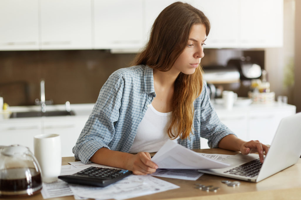 Beautiful Young Female Wearing Casual Shirt Calculating Family Budget, Looking Through Expenses While Managing Home Accounts, Paying Utility Bills Online Using Wifi On Generic Notebook Computer - OFFICE CONT - Contabilidade Digital para você e sua empresa